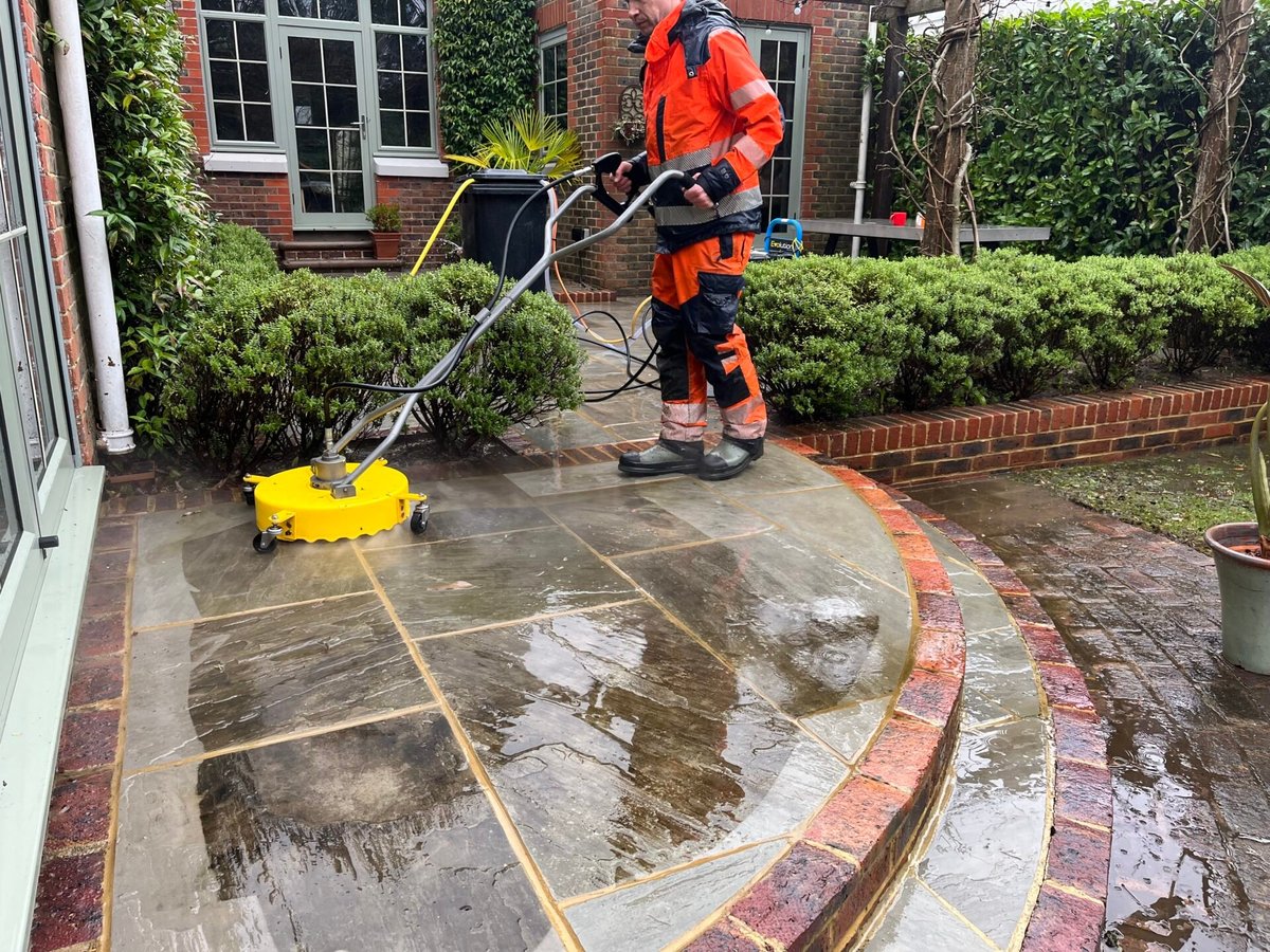 An Affa Fresh operator in hi-vis gear pressure washing a curved stone patio
